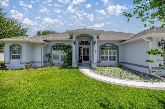 ranch-style home featuring a front yard, stucco siding, and roof with shingles
