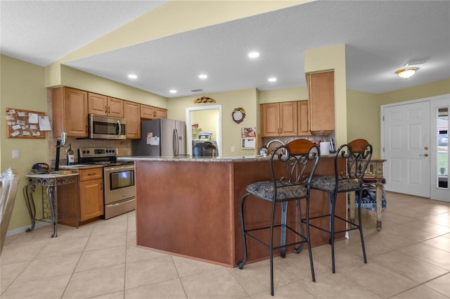 4692 N Lake Vista Trl, Hernando, FL 34442 - kitchen featuring stainless steel appliances, tasteful backsplash, a peninsula, brown cabinets, and a textured ceiling