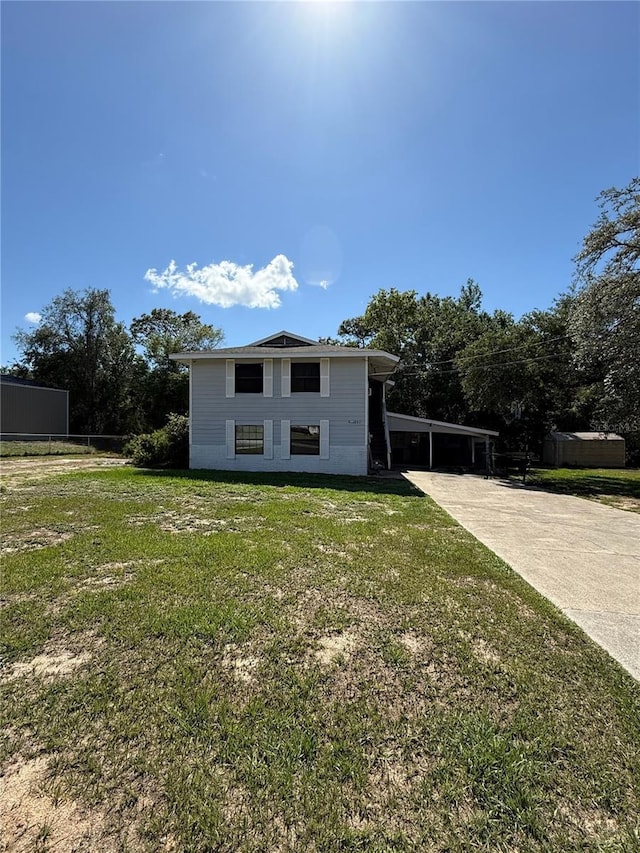 back of house featuring concrete driveway, a yard, and an attached carport