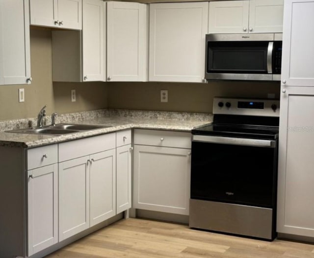 kitchen featuring appliances with stainless steel finishes, a sink, light wood-type flooring, light countertops, and white cabinets