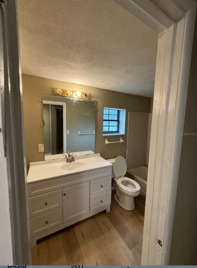 full bathroom with wood finished floors, a textured ceiling, vanity, a bathtub, and toilet