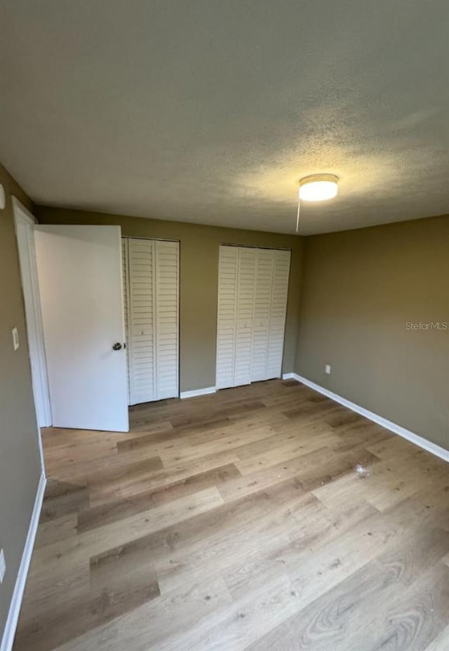 unfurnished bedroom with multiple closets, baseboards, wood finished floors, and a textured ceiling