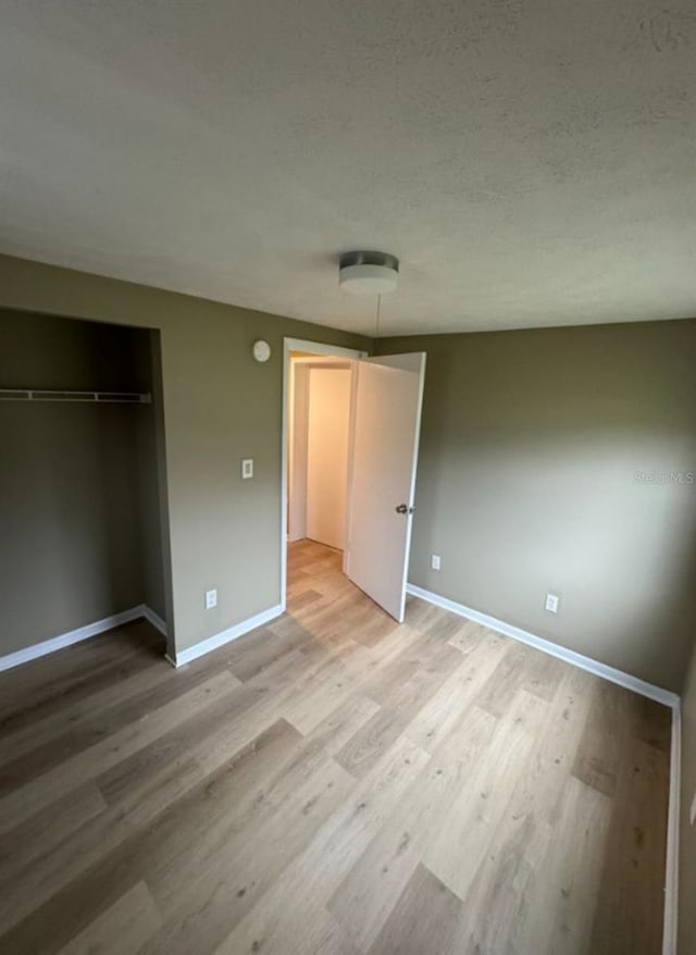 unfurnished bedroom featuring light wood-style floors, baseboards, a closet, and a textured ceiling