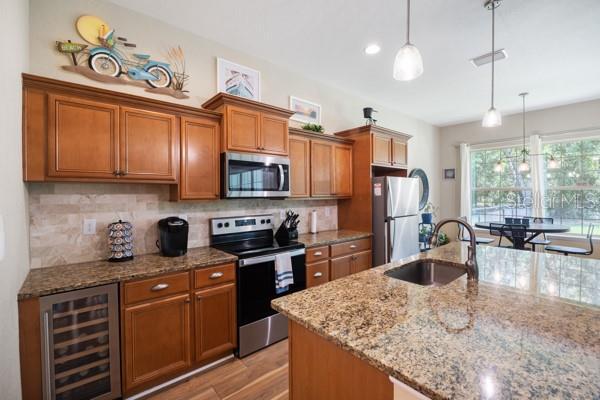 6235 SW 95th Pl, Ocala, FL 34476 - kitchen with stainless steel appliances, beverage cooler, a sink, brown cabinets, and decorative backsplash