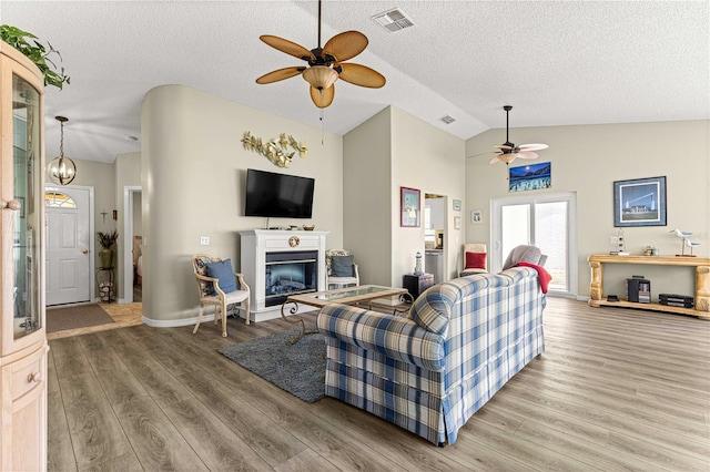 9266 SW 91st Cir, Ocala, FL 34481 - living area featuring ceiling fan, lofted ceiling, a glass covered fireplace, light wood-style floors, and a textured ceiling