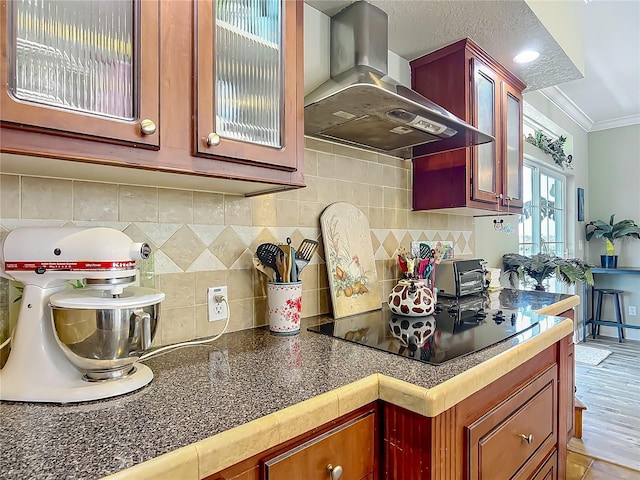1575 S Wallace Pt Unit 23, Crystal River, FL 34429 - kitchen featuring wall chimney range hood, black electric stovetop, tasteful backsplash, crown molding, and glass insert cabinets