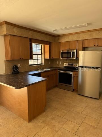 3740 NE 5th St, Ocala, FL 34470 - kitchen with stainless steel appliances, a peninsula, dark countertops, and brown cabinetry