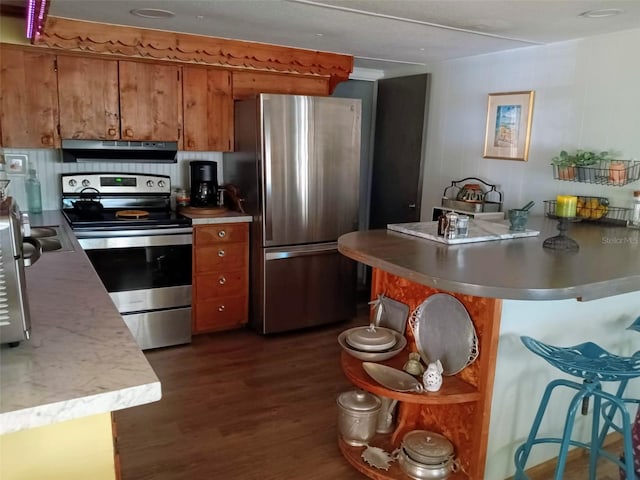 22736 SW 117th St, Dunnellon, FL 34431 - kitchen featuring appliances with stainless steel finishes, brown cabinets, under cabinet range hood, dark wood-style flooring, and a peninsula