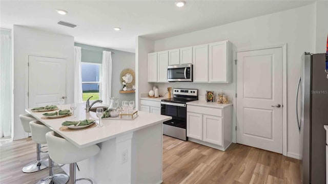 4937 SW 51st Rd, Gainesville, FL 32608 - kitchen featuring stainless steel appliances, a kitchen bar, white cabinets, a kitchen island with sink, and light wood finished floors