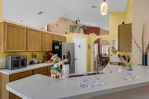2434 Walnut Heights Rd, Apopka, FL 32703 - kitchen with stainless steel fridge with ice dispenser, arched walkways, light countertops, a peninsula, and high vaulted ceiling