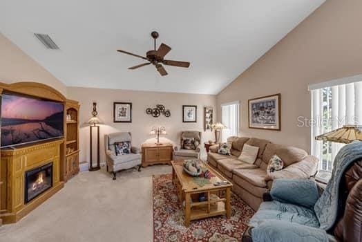 2434 Walnut Heights Rd, Apopka, FL 32703 - living area with vaulted ceiling, ceiling fan, plenty of natural light, light colored carpet, and a glass covered fireplace