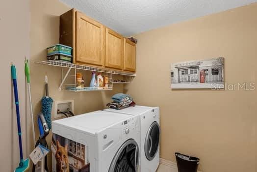2434 Walnut Heights Rd, Apopka, FL 32703 - laundry area featuring washer and clothes dryer, cabinet space, a textured ceiling, and baseboards