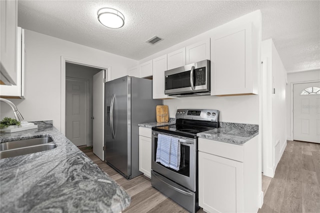4095 SW 144th St, Ocala, FL 34473 - kitchen featuring appliances with stainless steel finishes, a sink, light wood-style floors, a textured ceiling, and white cabinets