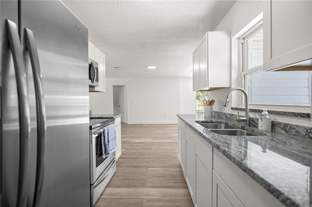 4095 SW 144th St, Ocala, FL 34473 - kitchen with stainless steel appliances, a sink, a textured ceiling, dark stone counters, and light wood-style floors