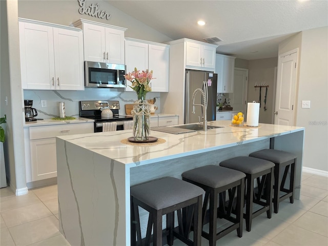 5667 SW 92nd Pl, Ocala, FL 34476 - kitchen with appliances with stainless steel finishes, light tile patterned flooring, white cabinets, a kitchen island with sink, and a kitchen breakfast bar