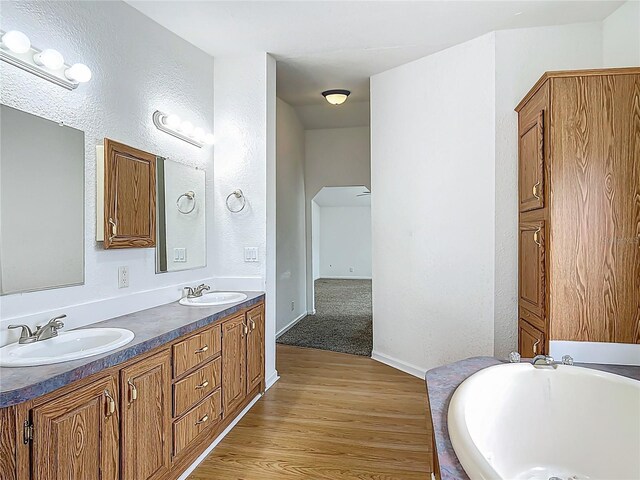 12352 SE 86th Ct, Belleview, FL 34420 - bathroom with double vanity, wood finished floors, a bath, a textured wall, and baseboards