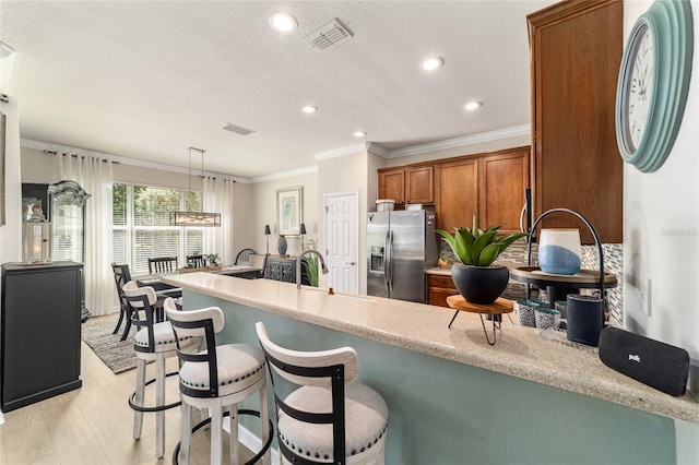 7263 SW 99th Cir, Ocala, FL 34481 - kitchen featuring stainless steel refrigerator with ice dispenser, brown cabinetry, a peninsula, ornamental molding, and light wood-style floors