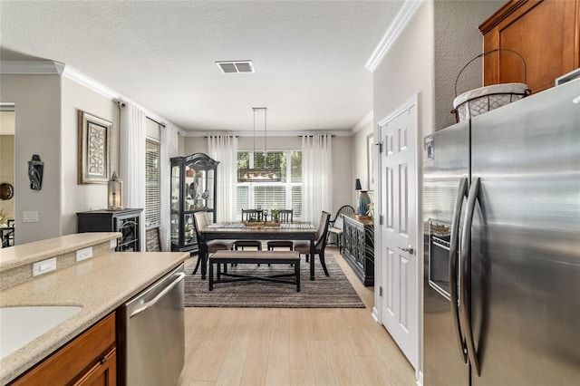 7263 SW 99th Cir, Ocala, FL 34481 - kitchen with appliances with stainless steel finishes, ornamental molding, brown cabinetry, light wood finished floors, and a textured ceiling