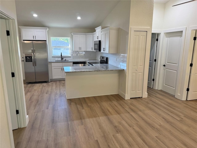14425 SW 21st Pl, Ocala, FL 34481 - kitchen featuring stainless steel appliances, a peninsula, light wood finished floors, tasteful backsplash, and light stone counters