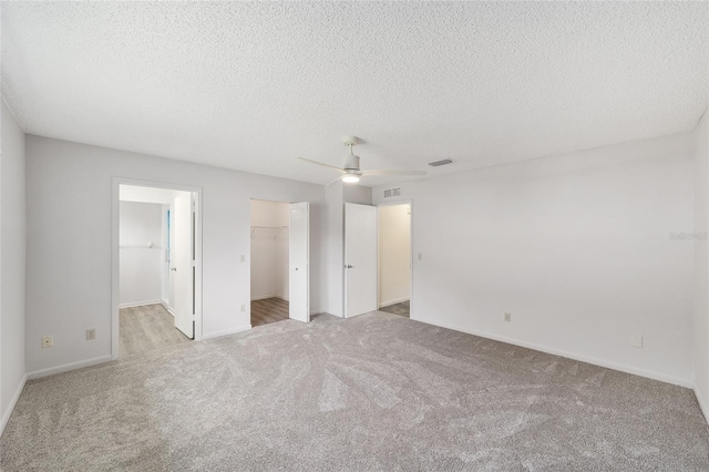 8998 SW 94th St Unit D, Ocala, FL 34481 - unfurnished bedroom with carpet flooring, a walk in closet, a textured ceiling, baseboards, and a ceiling fan