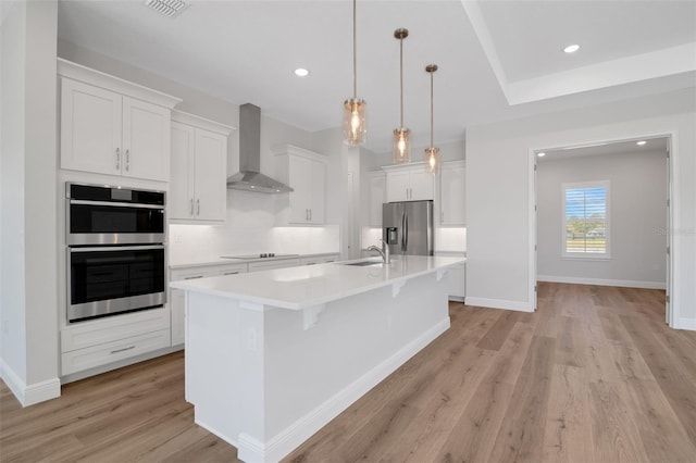 2050 NW 79th Loop, Ocala, FL 34475 - kitchen featuring stainless steel appliances, wall chimney range hood, light wood-style floors, a kitchen island with sink, and light countertops