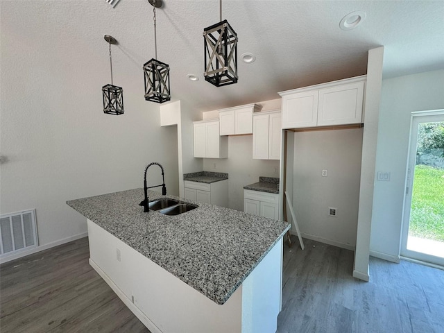 5709 NW 6th Pl, Ocala, FL 34482 - kitchen with white cabinetry, wood finished floors, an island with sink, stone countertops, and hanging light fixtures