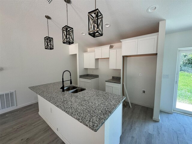 5701 NW 6th Pl, Ocala, FL 34482 - kitchen with white cabinetry, wood finished floors, an island with sink, stone countertops, and hanging light fixtures