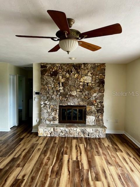 8770 SW 196th Terrace Rd, Dunnellon, FL 34432 - unfurnished living room with baseboards, wood finished floors, a stone fireplace, and ceiling fan