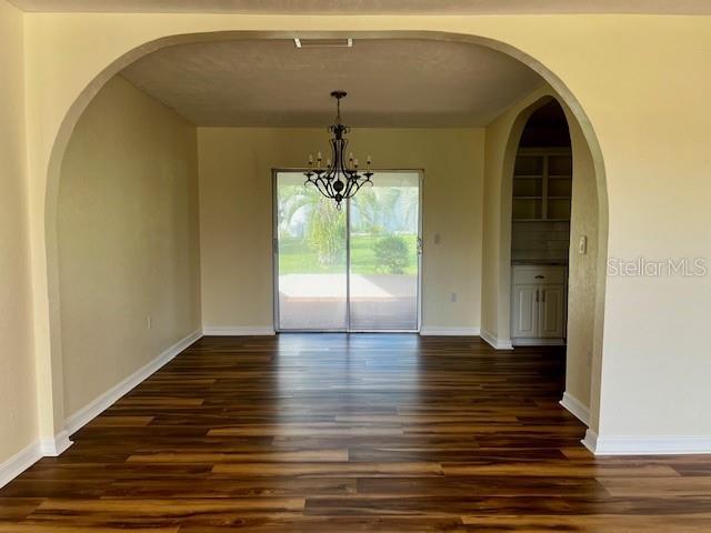 8770 SW 196th Terrace Rd, Dunnellon, FL 34432 - unfurnished dining area featuring dark wood-style floors, a chandelier, baseboards, and arched walkways
