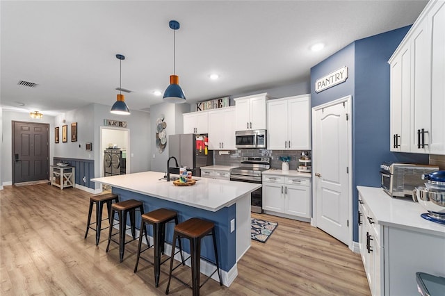 7479 SW 130th Ln, Ocala, FL 34473 - kitchen featuring stainless steel appliances, a breakfast bar area, light wood-style floors, decorative backsplash, and white cabinetry