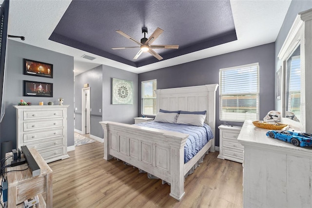 7479 SW 130th Ln, Ocala, FL 34473 - bedroom featuring a tray ceiling, a textured ceiling, light wood-type flooring, and multiple windows
