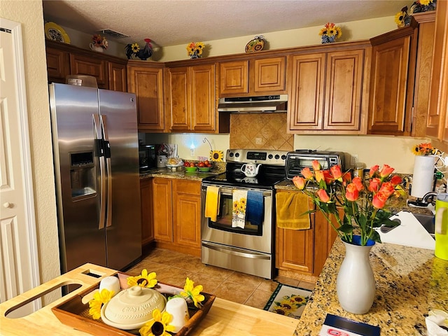 27 Cedar Tree Ter, Ocala, FL 34472 - kitchen featuring under cabinet range hood, appliances with stainless steel finishes, light tile patterned floors, brown cabinets, and backsplash