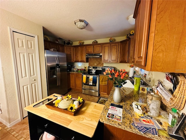 27 Cedar Tree Ter, Ocala, FL 34472 - kitchen featuring stainless steel appliances, under cabinet range hood, light tile patterned flooring, brown cabinetry, and a textured ceiling