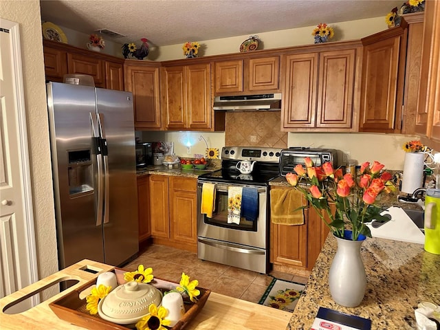27 Cedar Tree Ter, Ocala, FL 34472 - kitchen featuring under cabinet range hood, stainless steel appliances, brown cabinets, light tile patterned floors, and decorative backsplash