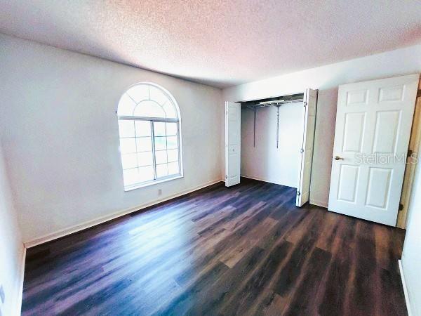 5110 NW 19th Pl, Ocala, FL 34482 - unfurnished bedroom with dark wood-type flooring, a textured ceiling, a closet, and baseboards