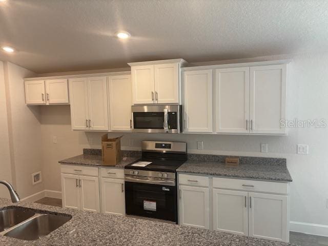 7637 SW 180th Cir, Dunnellon, FL 34432 - kitchen with stainless steel appliances, a sink, baseboards, white cabinets, and a textured ceiling