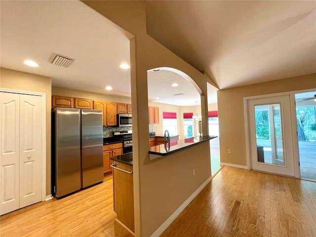 16405 SW 14th Avenue Rd, Ocala, FL 34473 - kitchen featuring stainless steel appliances, dark countertops, light wood-type flooring, decorative backsplash, and arched walkways