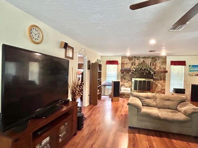 20100 SW 95th St, Dunnellon, FL 34431 - living room with wood finished floors, a ceiling fan, a stone fireplace, and a textured ceiling