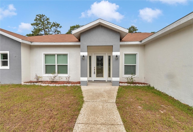 14550 SW 61st Ct, Ocala, FL 34473 - view of exterior entry featuring stucco siding, a yard, and roof with shingles