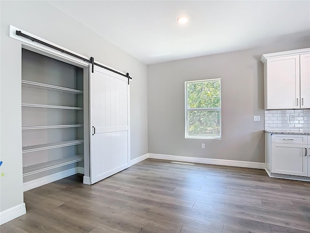 3018 Oceanside St, North Port, FL 34286 - unfurnished bedroom featuring a barn door, wood finished floors, and baseboards