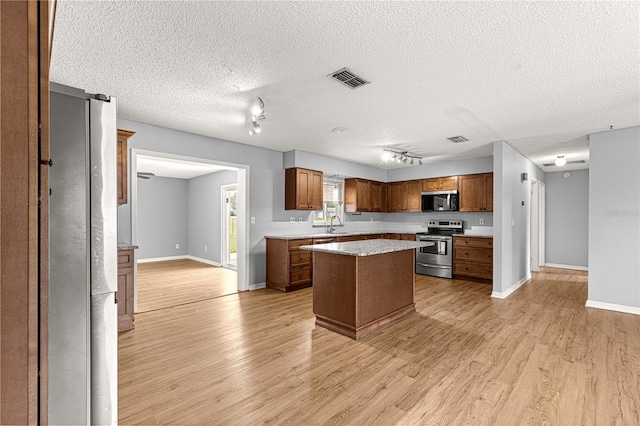 6989 SE 52nd Pl, Ocala, FL 34472 - kitchen featuring stainless steel appliances, light wood-type flooring, a center island, brown cabinetry, and a textured ceiling