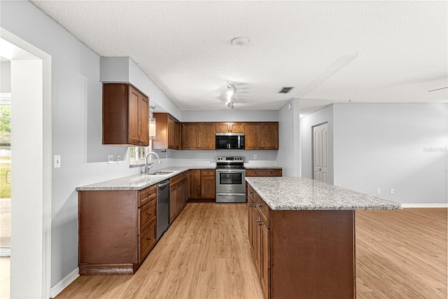6989 SE 52nd Pl, Ocala, FL 34472 - kitchen with appliances with stainless steel finishes, a sink, light wood-style floors, a kitchen island, and a textured ceiling