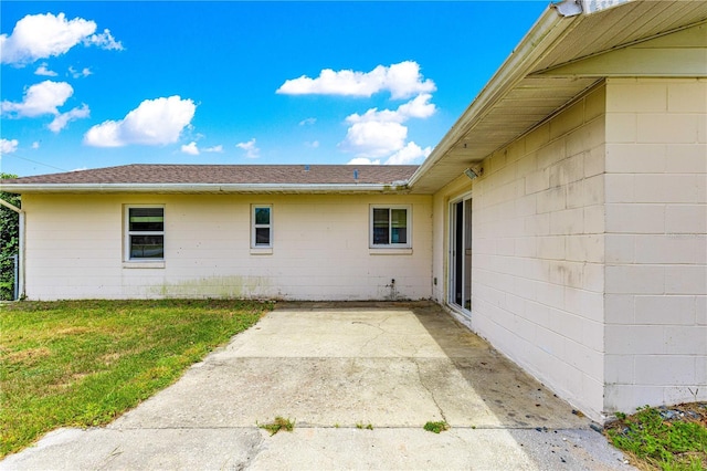6989 SE 52nd Pl, Ocala, FL 34472 - view of home's exterior with concrete block siding, a patio, a lawn, and a shingled roof