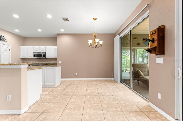8961 SE 130th Loop, Summerfield, FL 34491 - kitchen with stainless steel microwave, a chandelier, white cabinets, light stone counters, and decorative light fixtures