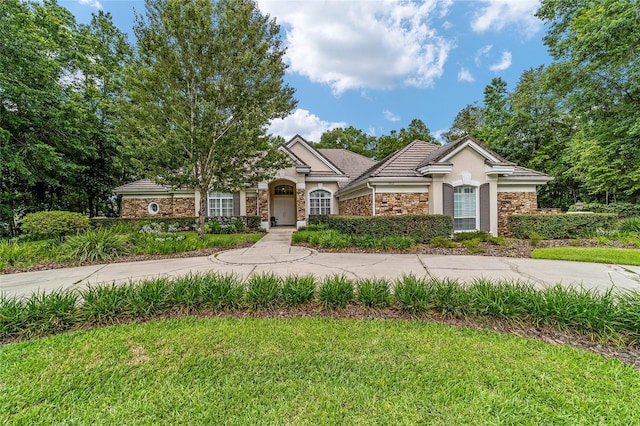 7915 SE 12th Cir, Ocala, FL 34480 - view of front facade featuring stone siding, stucco siding, a front lawn, and a tile roof