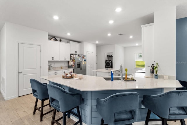 19551 SW 77th Loop, Dunnellon, FL 34432 - kitchen with stainless steel fridge with ice dispenser, white cabinets, washer / dryer, a kitchen breakfast bar, and light wood-style flooring