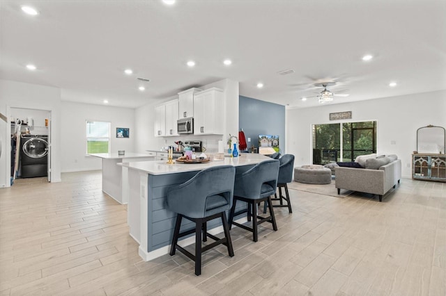 19551 SW 77th Loop, Dunnellon, FL 34432 - kitchen with appliances with stainless steel finishes, washer / dryer, white cabinetry, light wood finished floors, and light countertops