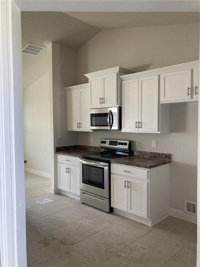 2 Pine Course Trl, Ocala, FL 34472 - kitchen with stainless steel appliances, vaulted ceiling, white cabinetry, dark countertops, and baseboards