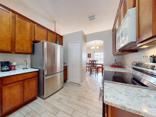 8080 N Susan Ave, Dunnellon, FL 34433 - kitchen with appliances with stainless steel finishes, brown cabinetry, arched walkways, and a chandelier