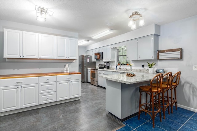 126 SW Mockingbird Way, Lake City, FL 32024 - kitchen with appliances with stainless steel finishes, a peninsula, a breakfast bar, a textured ceiling, and baseboards